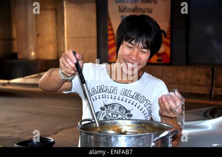 Bangkok, Thailandia: Thai sorridente uomo vendita zuppa calda da un grande calderone di metallo al suo portatile food cart in Silom Road Foto Stock