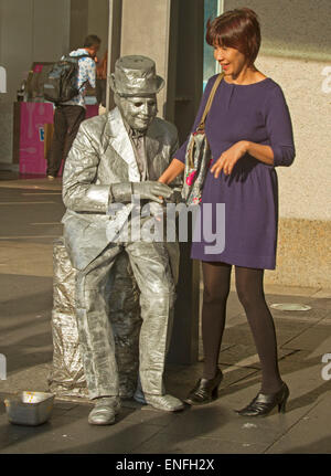 L'uomo musicista di strada come statua vivente con corpo argento, vestiti e hat interagenti con sorridente donna asiatica al Circular Quay di Sydney Australia Foto Stock