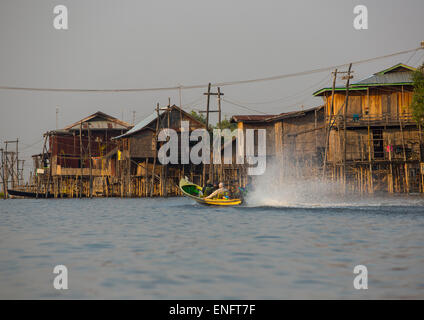 Barca dalla coda lunga passando davanti ad una tipica casa su palafitte, Lago Inle, Myanmar Foto Stock