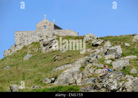 St Ives, Cornovaglia: giovani donne in vestito blu rilassante sulle rocce a St Ives in Cornovaglia con St Nicholas' cappella dietro Foto Stock