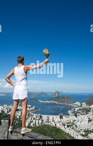 Un vecchio stile atleta in sport uniforme tenendo permanente sport torcia presso skyline della città si affacciano sul Rio de Janeiro in Brasile Foto Stock