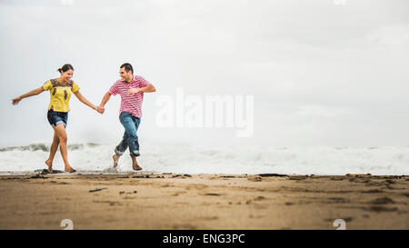 Coppia ispanica in esecuzione in onde sulla spiaggia Foto Stock