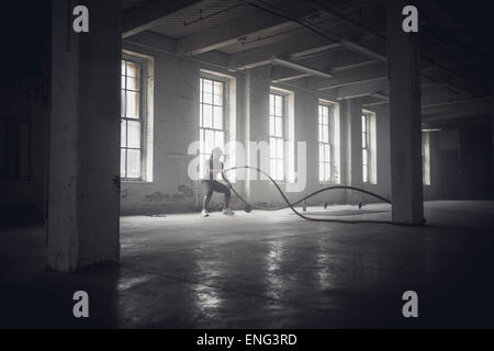 Nero donna tossing funi nel buio della palestra Foto Stock