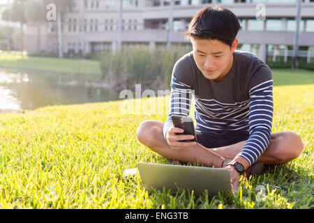 Il coreano Uomo con laptop e telefono cellulare in erba Foto Stock