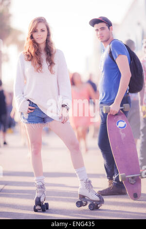 Donna su pattini a rotelle con guidatore di skateboard sul marciapiede Foto Stock