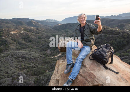 Vecchio uomo caucasico tenendo cellulare fotografia sulla collina rocciosa Foto Stock