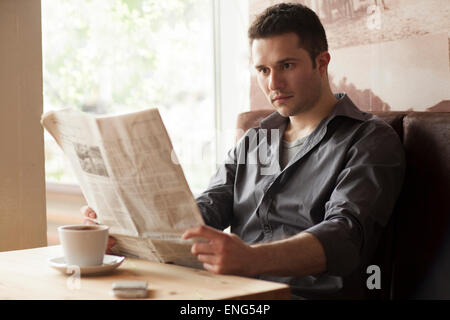 Uomo che legge il giornale e bere il caffè nella caffetteria Foto Stock