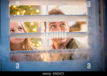 Caucasian padre e figlia del peering fuori la finestra il pupazzo di neve a Natale Foto Stock