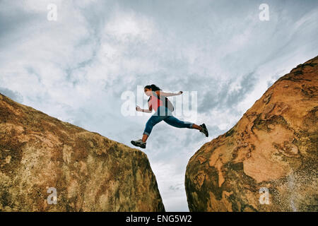 Donna ispanica jumping crepaccio sulle formazioni rocciose Foto Stock