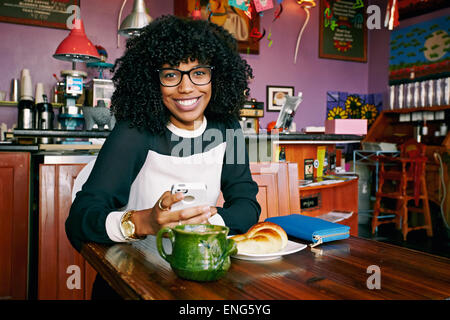 Razza mista donna utilizzando il cellulare in cafe Foto Stock
