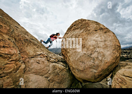 Donna ispanica spingendo boulder sulla collina rocciosa Foto Stock