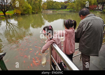 Le ragazze e il loro nonno nutrono la carpa koi nel Guangchang Park, vicino a Xintiandi, a Shanghai, Cina. Foto Stock