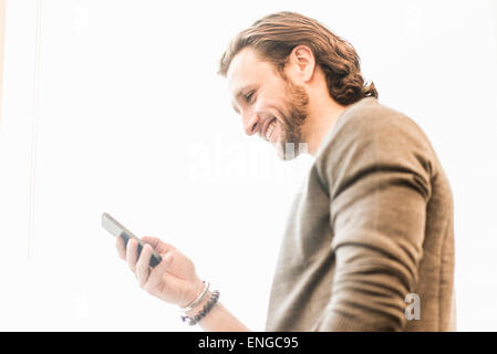 Un barbuto uomo sorridente e controllando il suo telefono. Foto Stock