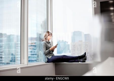 Una donna in possesso di una smart phone, seduto su un davanzale. Foto Stock