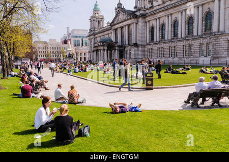 Molte persone godendo il sole a Belfast City Hall Foto Stock
