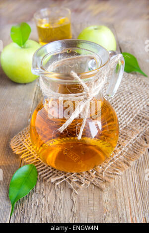 Il succo di mela (sidro) in caraffa con mele verdi e foglie sul rustico sfondo di legno Foto Stock