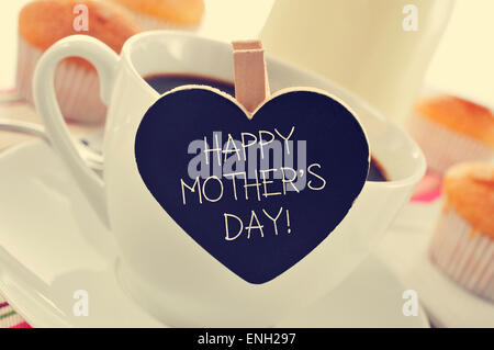 La frase felice festa della mamma scritto in una a forma di cuore di blackboard collocato in una tazza di caffè, con qualche muffin in backgrou Foto Stock