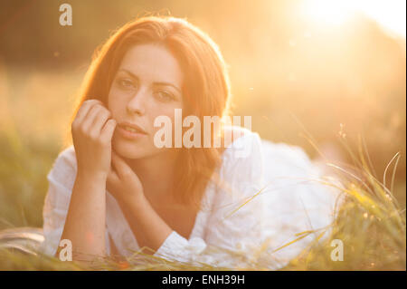 Giovane donna con capelli auburn posa in un campo illuminate dal sole al tramonto Foto Stock