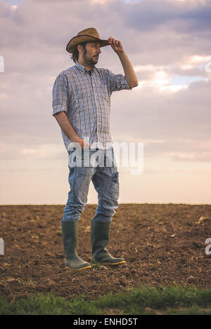 Ritratto di maschio adulto agricoltore permanente sulla fertile terreno agricolo terreno,cercando in distanza. Foto Stock