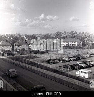 1950, vista panoramica storica delle auto dell'epoca parcheggiate su un terreno vuoto accanto a una strada in un'area suburbana del sud di Londra, Inghilterra, Regno Unito. Il terreno del parcheggio ha una superficie liscia ed è recintato. Foto Stock