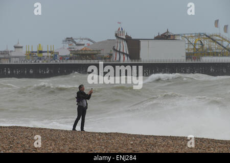 Un uomo prende una fotografia delle grandi onde, provocata da una tempesta, schiantati sulla spiaggia di fronte al molo di Brighton a Brighton, East Sussex, Inghilterra. Foto Stock