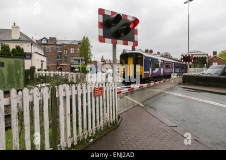 A nord del convoglio ferroviario passa attraverso un passaggio a livello a Hale , Greater Manchester Foto Stock