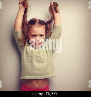 Active infelice emozione kid ragazza tirando i suoi lunghi capelli a. Vintage closeup ritratto Foto Stock