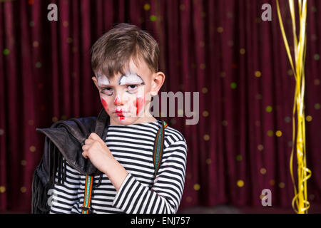 Sulky piccolo ragazzo che indossa la faccia della vernice sul palco guardando la telecamera con un soulful triste espressione come egli si trova di fronte la cu Foto Stock