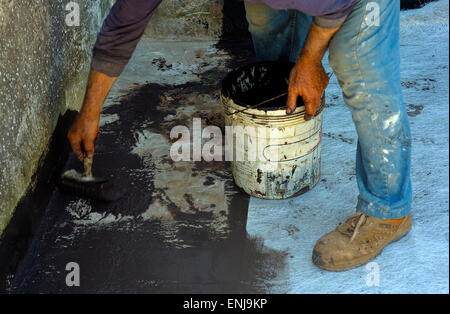 Lavoratore in posa con spazzola guaina bituminosa liquido sul foglio di fibra di vetro Foto Stock