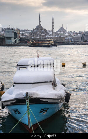 Coperte di neve sulla barca Karakoy waterfront, guardando attraverso il Golden Horn verso la moschea Yeni a Eminonu e Istanbul skyl Foto Stock