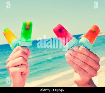 Primo piano delle mani di un giovane uomo caucasico con alcuni fatti in casa pop di ghiaccio con sapori diversi sulla spiaggia, con un filtro effe Foto Stock