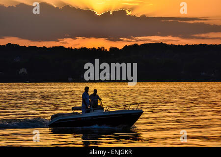 Suggestivo tramonto sul Lago di Starnberg vicino a Schloss Berg con la silhouette di un motoscafo e la riflessione del sole Foto Stock