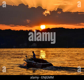 Suggestivo tramonto sul Lago di Starnberg vicino a Schloss Berg con la silhouette di un motoscafo e la riflessione del sole Foto Stock