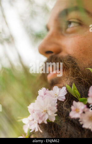 Fiori decorano la barba di questo giovane uomo per godersi la natura Foto Stock