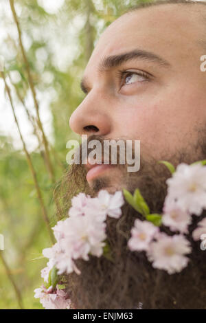 Fiori decorano la barba di questo giovane uomo per godersi la natura Foto Stock