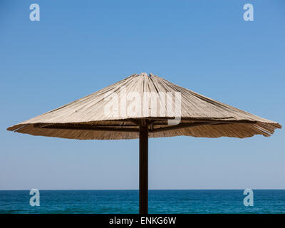 La parte superiore di una singola aletta parasole di paglia contro il blu del cielo e del mare. Foto Stock