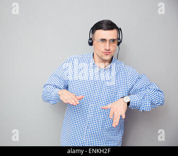 Ritratto di un uomo elegante in bicchieri e cuffie ballando su sfondo grigio Foto Stock