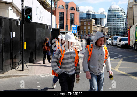 Lavoratori provenienti da siti di costruzione a piedi lungo la strada strada della città con una vista di Bezier Appartamenti Londra E1 UK KATHY DEWITT Foto Stock