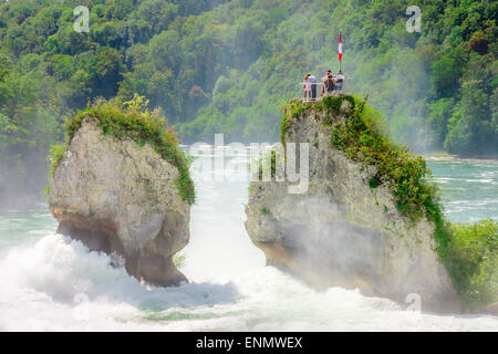 Gruppo di turisti che sperimentano lo splendore naturale dalla cima di un affioramento roccioso presso le cascate del Reno, la più grande cascata della Svizzera Foto Stock