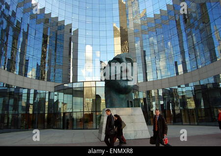 Una statua in bronzo del capo di un uomo circondato da un moderno, vetro edificio per uffici. Foto Stock