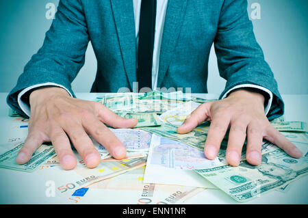 Primo piano di un giovane uomo caucasico in tuta seduto alla sua scrivania piena di euro e le fatture del dollaro cercando di tenerli, raffiguranti Foto Stock