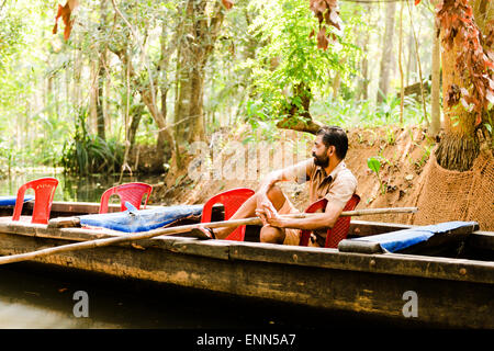 Un barcaiolo guida turistica avente un po' di riposo in attesa per i suoi passeggeri a tornare in Kerala Backwaters. Foto Stock