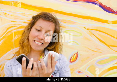 Felice ragazza guardando due telefoni intelligenti contro uno sfondo colorato Foto Stock