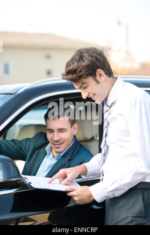 Rivenditore di auto e il giovane uomo firma un contratto Foto Stock