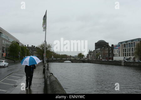 Un Uomo con ombrello passeggiate lungo le banchine del fiume Liffey. Immagine dal centro della città di Dublino durante un periodo di forte pioggia Foto Stock