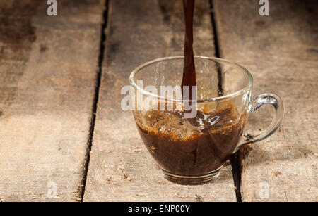 Versare il caffè nella tazza di vetro sul vecchio sfondo di legno. Foto Stock