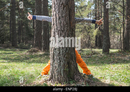 Il bambino gioca nella foresta nascosta dietro un albero Foto Stock