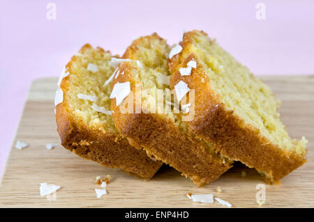 Fette di fatto in casa torta di noce di cocco sul tagliere contro un sfondo rosa Foto Stock