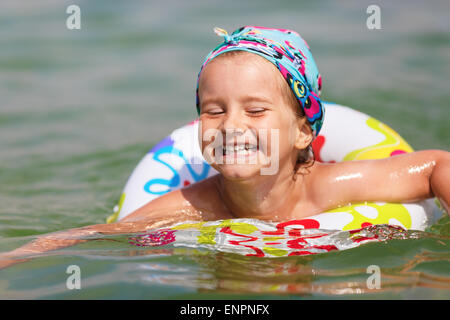Bambino felice nuota nel mare su anello gonfiabile in una limpida giornata di sole. Profondità di campo. Attenzione sul modello del viso. Foto Stock