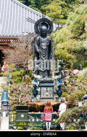 Il tempio Kiyoshikōjin Seichō-ji a Takarazuka, Giappone. Donna in piedi di fronte alla statua di kannon e getta l'acqua ad essa mentre pregava. Foto Stock